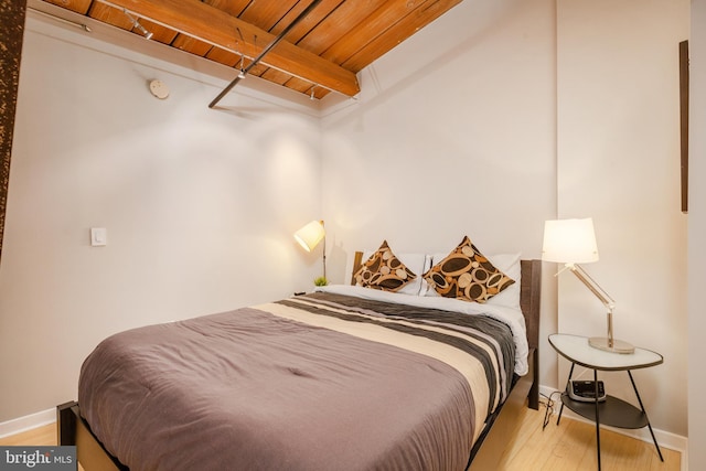 bedroom with light hardwood / wood-style floors, beam ceiling, and wooden ceiling