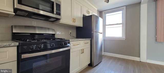 kitchen with white cabinets, light stone counters, stainless steel appliances, and light hardwood / wood-style flooring