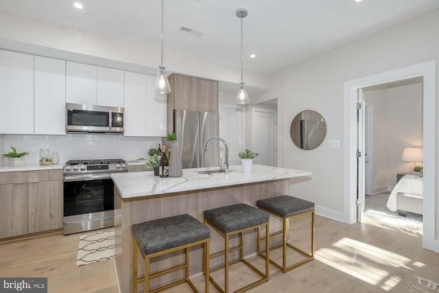 kitchen with pendant lighting, appliances with stainless steel finishes, an island with sink, and white cabinets