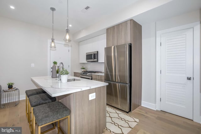 kitchen featuring appliances with stainless steel finishes, pendant lighting, sink, white cabinets, and a center island with sink