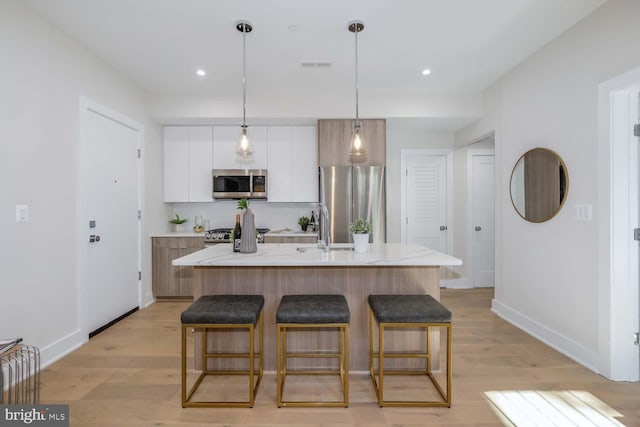 kitchen with light hardwood / wood-style flooring, white cabinetry, hanging light fixtures, a kitchen island with sink, and stainless steel appliances