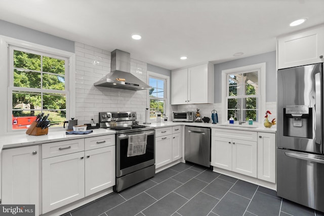 kitchen with appliances with stainless steel finishes, tasteful backsplash, white cabinetry, sink, and wall chimney exhaust hood