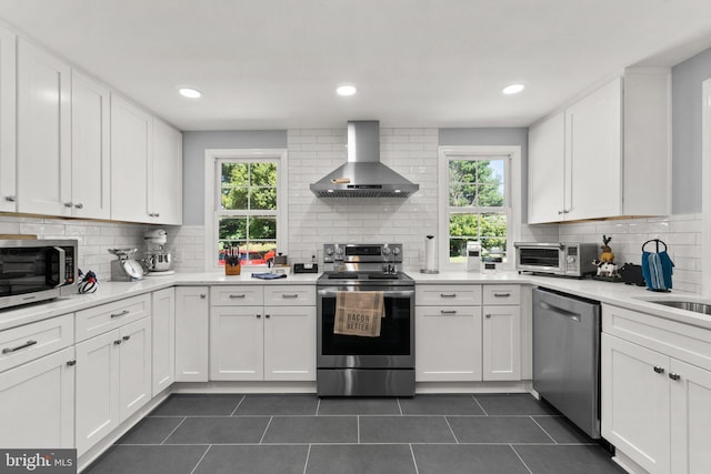 kitchen featuring appliances with stainless steel finishes, tasteful backsplash, white cabinets, dark tile patterned flooring, and wall chimney exhaust hood