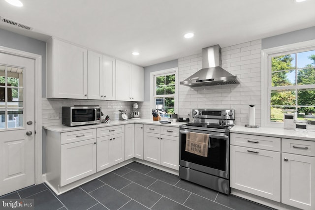 kitchen featuring tasteful backsplash, white cabinets, dark tile patterned flooring, stainless steel appliances, and wall chimney range hood