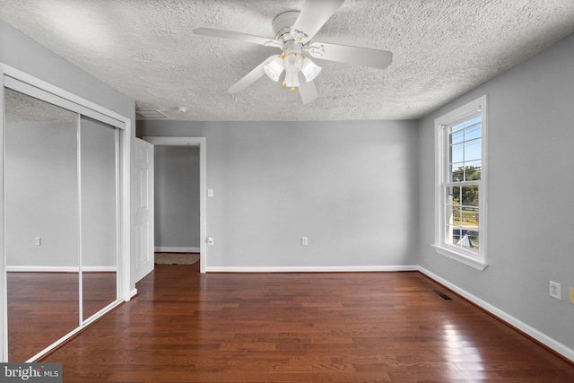 unfurnished bedroom with ceiling fan, dark wood-type flooring, a textured ceiling, and a closet