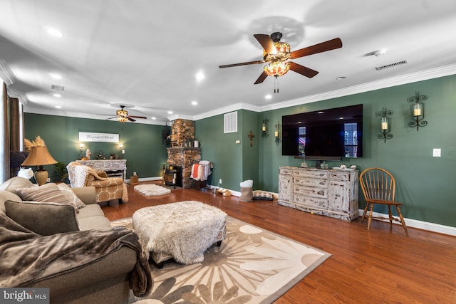 living room with ceiling fan, ornamental molding, a stone fireplace, and hardwood / wood-style floors