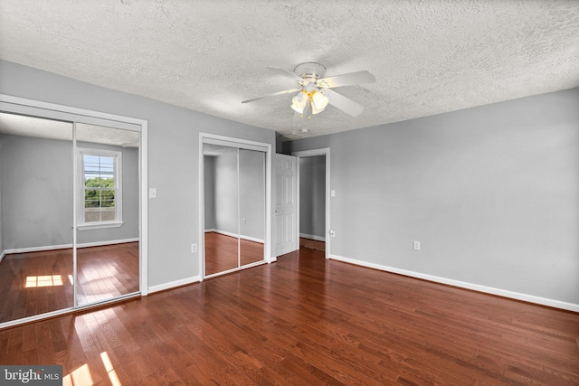 unfurnished bedroom with ceiling fan, dark hardwood / wood-style floors, two closets, and a textured ceiling