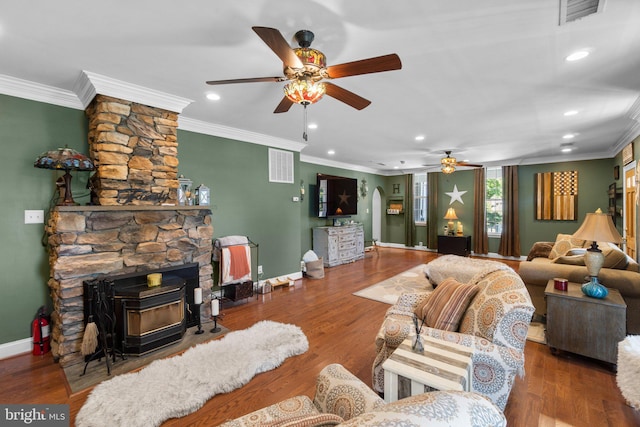 living room with crown molding, ceiling fan, wood-type flooring, and a wood stove