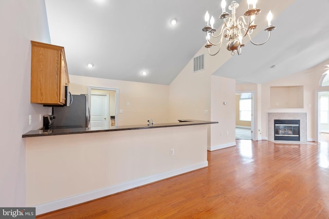 kitchen featuring kitchen peninsula, light wood-type flooring, ceiling fan with notable chandelier, pendant lighting, and high vaulted ceiling