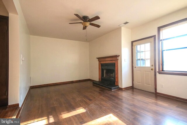 unfurnished living room with dark hardwood / wood-style flooring, ceiling fan, and a tiled fireplace