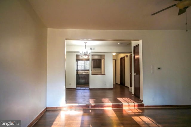 spare room featuring ceiling fan with notable chandelier and dark wood-type flooring