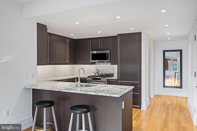 kitchen featuring kitchen peninsula, dark brown cabinets, light hardwood / wood-style floors, and appliances with stainless steel finishes