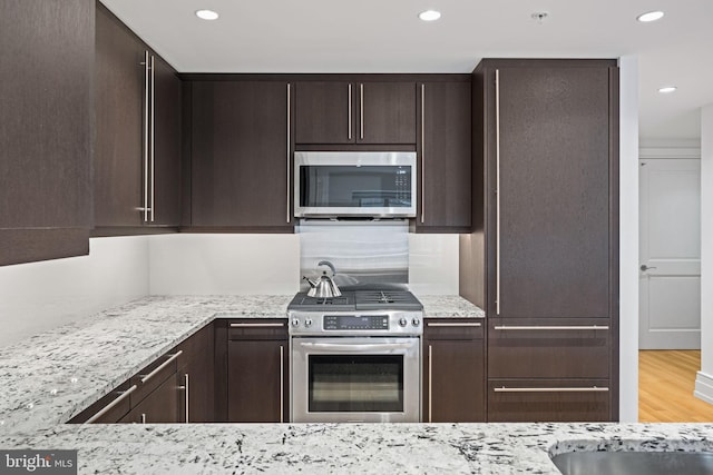 kitchen with dark brown cabinetry, light stone countertops, light hardwood / wood-style flooring, and stainless steel appliances