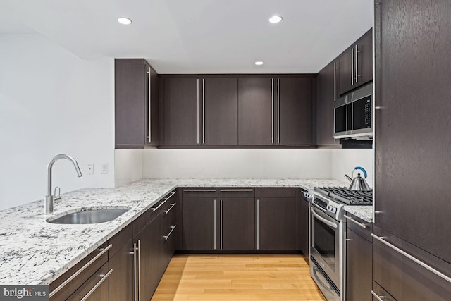 kitchen with appliances with stainless steel finishes, light wood-type flooring, light stone counters, dark brown cabinetry, and sink