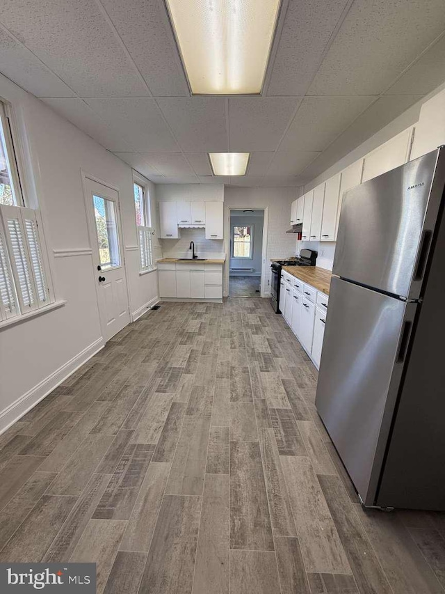 kitchen featuring white cabinetry, butcher block counters, stainless steel fridge, and plenty of natural light