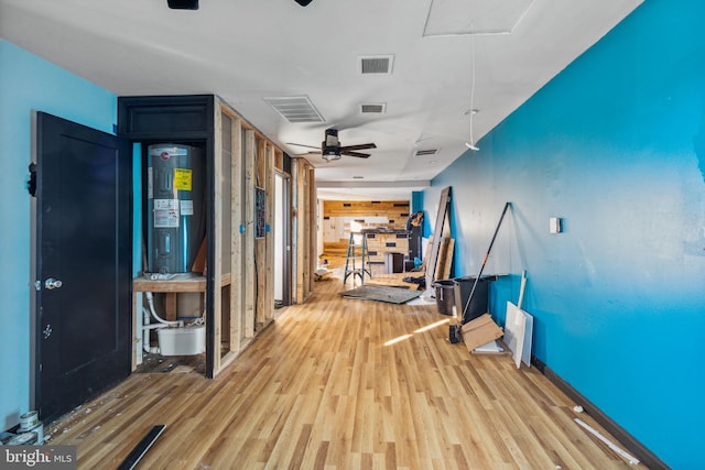 corridor with wood walls, electric water heater, and light hardwood / wood-style flooring