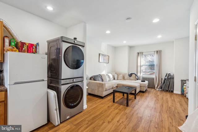 laundry area featuring stacked washer and dryer, radiator, and light hardwood / wood-style flooring