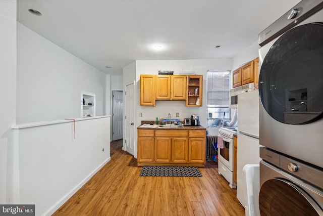 kitchen featuring stainless steel oven, white range, sink, light hardwood / wood-style flooring, and stacked washer / dryer