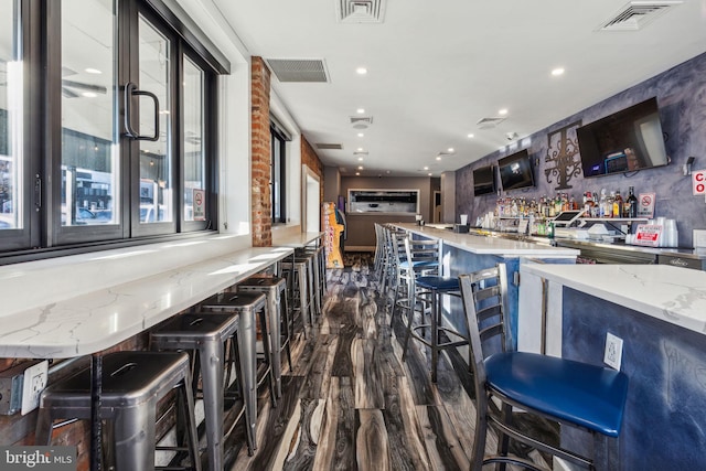 bar with light stone countertops and dark wood-type flooring