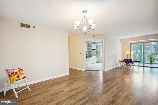 unfurnished room with hardwood / wood-style floors, a textured ceiling, and an inviting chandelier