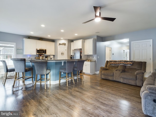 kitchen featuring white cabinetry, ceiling fan, a breakfast bar, appliances with stainless steel finishes, and hardwood / wood-style flooring