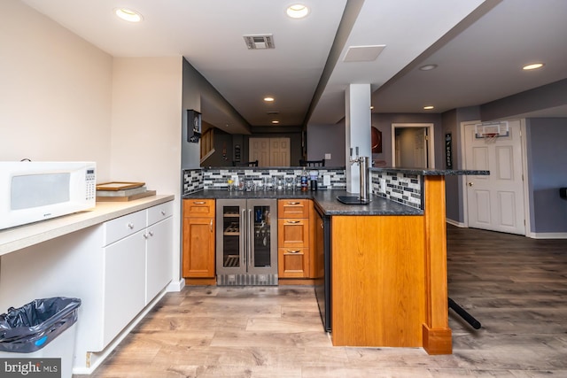 kitchen featuring backsplash, light wood-type flooring, kitchen peninsula, a breakfast bar area, and beverage cooler