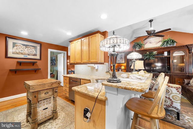 kitchen featuring ceiling fan, vaulted ceiling, light hardwood / wood-style floors, decorative backsplash, and light stone counters