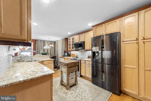 kitchen with decorative light fixtures, stainless steel appliances, tasteful backsplash, sink, and light hardwood / wood-style flooring