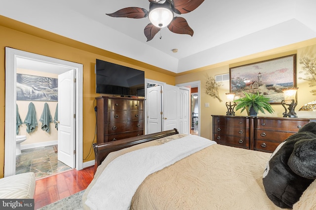 bedroom featuring ceiling fan, connected bathroom, hardwood / wood-style flooring, and a tray ceiling