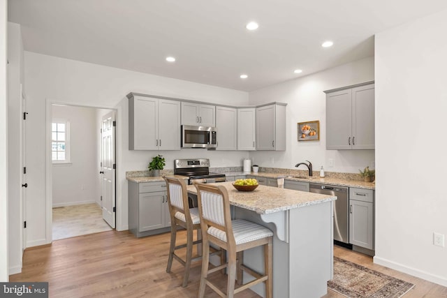 kitchen with gray cabinets, light wood-type flooring, appliances with stainless steel finishes, a kitchen island, and light stone counters