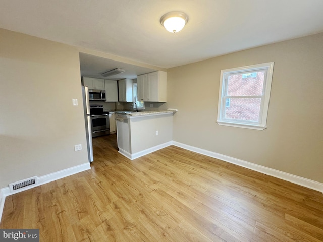 kitchen with sink, light hardwood / wood-style flooring, kitchen peninsula, white cabinets, and appliances with stainless steel finishes