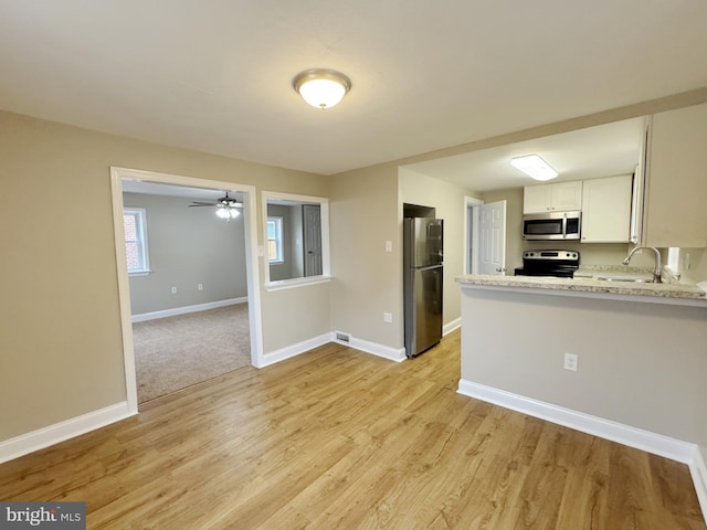 kitchen with sink, light stone countertops, light hardwood / wood-style floors, white cabinetry, and stainless steel appliances