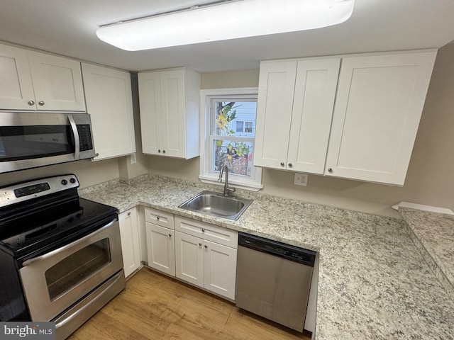 kitchen with appliances with stainless steel finishes, light hardwood / wood-style floors, white cabinetry, and sink