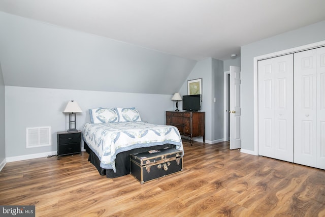 bedroom with hardwood / wood-style flooring, lofted ceiling, and a closet