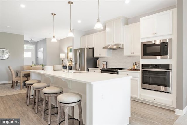 kitchen with hanging light fixtures, appliances with stainless steel finishes, light hardwood / wood-style floors, and a kitchen island with sink