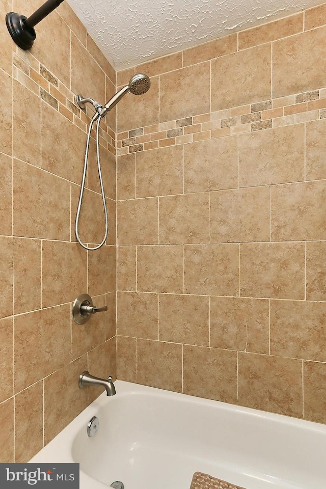 bathroom featuring a textured ceiling and tiled shower / bath