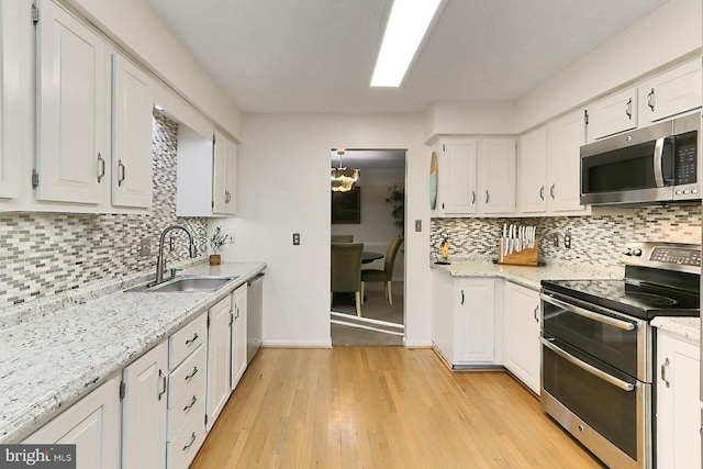 kitchen with tasteful backsplash, white cabinets, light hardwood / wood-style floors, and appliances with stainless steel finishes