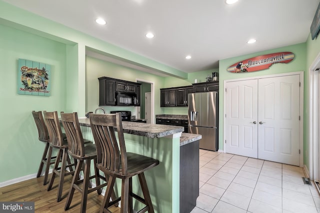 143 Mayor Ln, Felton, DE 19943 - kitchen with stainless steel fridge with ice dispenser, black microwave, a peninsula, a breakfast bar area, and electric range oven