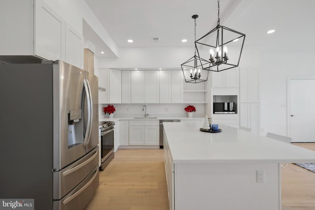 kitchen with hanging light fixtures, sink, appliances with stainless steel finishes, a kitchen island, and white cabinetry