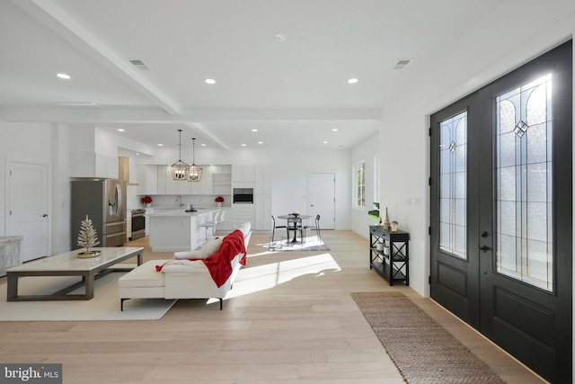 entrance foyer featuring beam ceiling, light wood-type flooring, a wealth of natural light, and an inviting chandelier