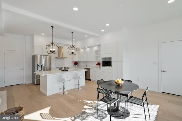 kitchen featuring wall chimney exhaust hood, appliances with stainless steel finishes, decorative light fixtures, a kitchen island, and white cabinetry