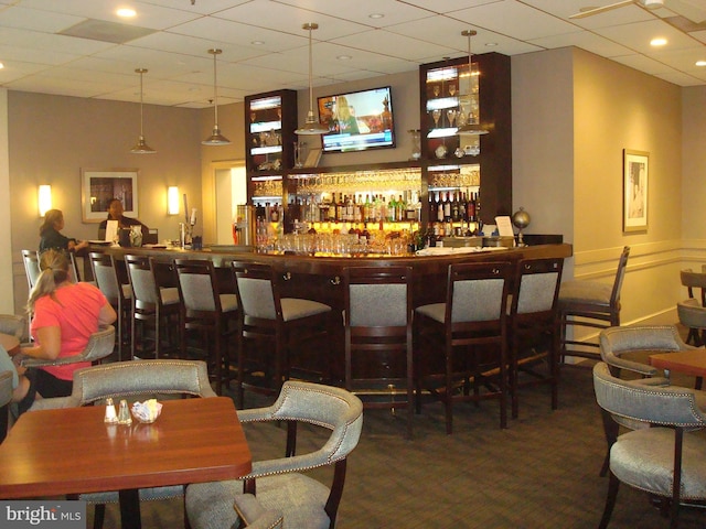 bar featuring a paneled ceiling, dark carpet, and hanging light fixtures