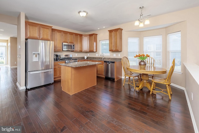 kitchen featuring pendant lighting, dark hardwood / wood-style floors, light stone countertops, appliances with stainless steel finishes, and a kitchen island