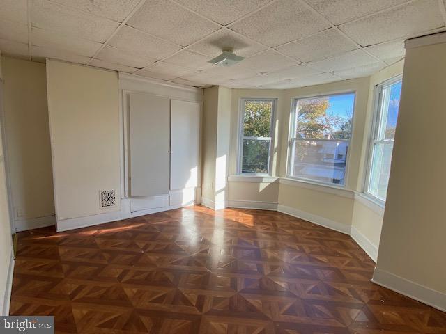 empty room featuring a drop ceiling and dark parquet floors