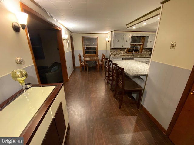 kitchen with white cabinets, a kitchen breakfast bar, backsplash, and dark hardwood / wood-style floors