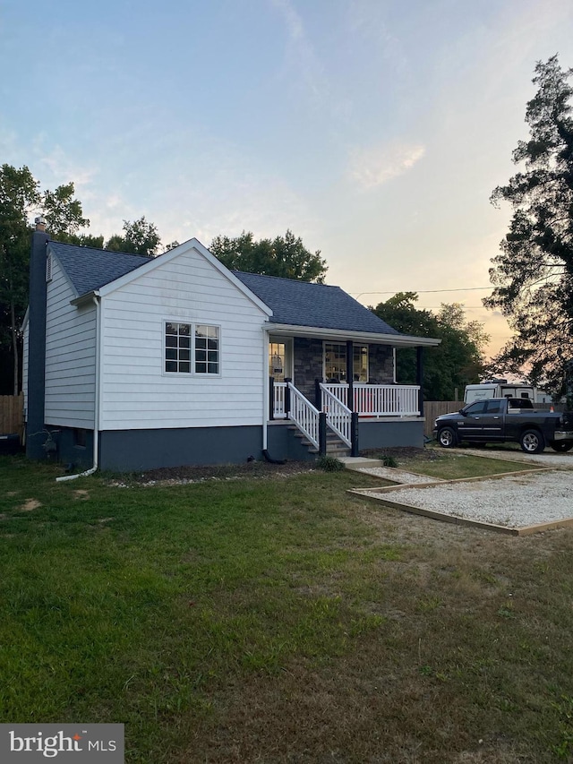 ranch-style home with covered porch, a yard, and roof with shingles