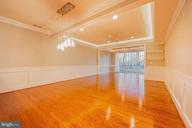 empty room with wood-type flooring, ceiling fan with notable chandelier, and crown molding