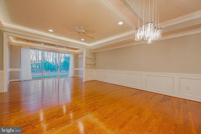 unfurnished room with ceiling fan with notable chandelier, wood-type flooring, ornamental molding, and a tray ceiling