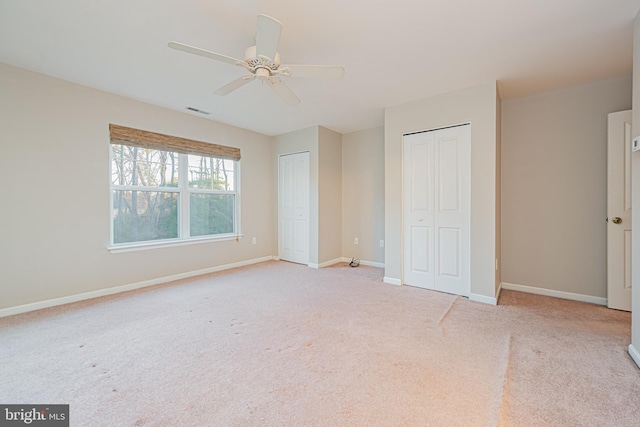 unfurnished bedroom with light colored carpet, ceiling fan, and multiple closets