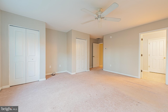 unfurnished bedroom with ceiling fan, light carpet, and two closets